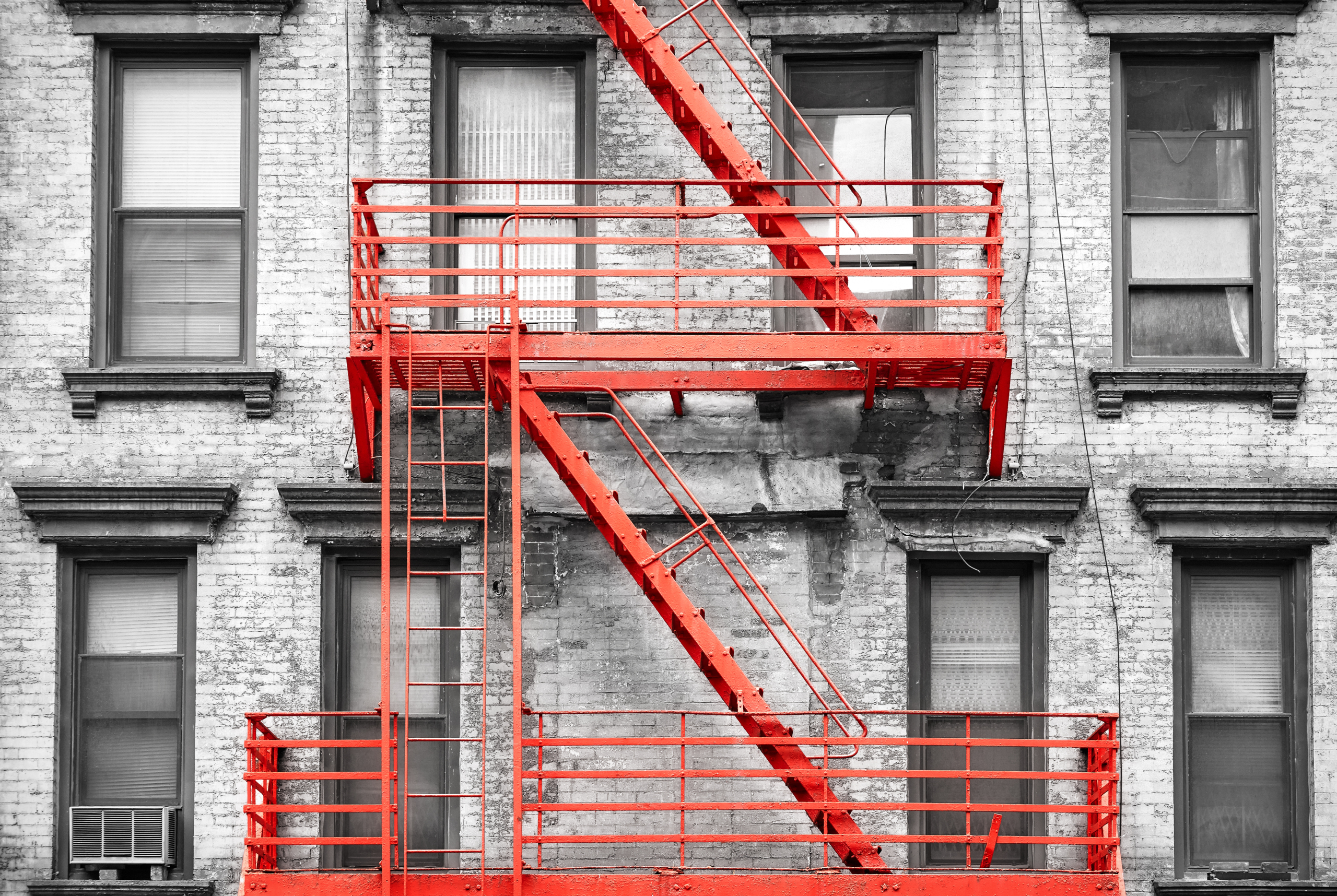 Red fire escape at black and white filtered residential building, NYC.