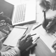 A group of people gathered around a table going over paper work with phones and laptops on hand