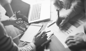 A group of people gathered around a table going over paper work with phones and laptops on hand